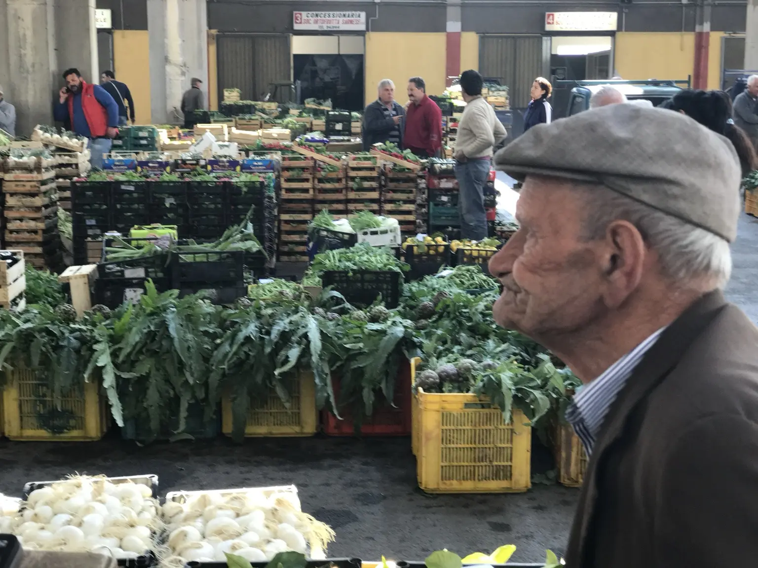 Profilo di un anziano produttore tra verdure e cassette del mercato
